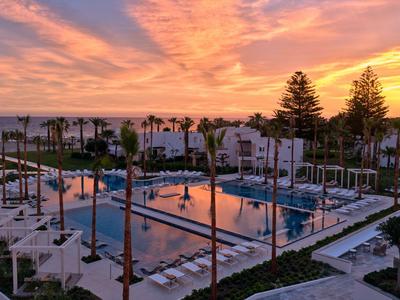 Piscina dell'hotel con lettini e palme al tramonto.