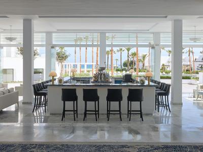 Zona lounge moderna dell’hotel con bar, sgabelli alti e vista sul mare attraverso grandi finestre.