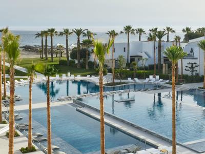 Moderna area piscina con palme e edifici bianchi vicino al mare in un resort.