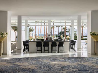 Elegante bar dell'hotel con vista su palme e mare attraverso grandi finestre.