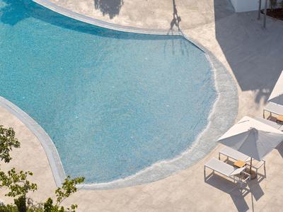 Acqua chiara bluastra in una piscina con sedie a sdraio e ombre sullo sfondo.