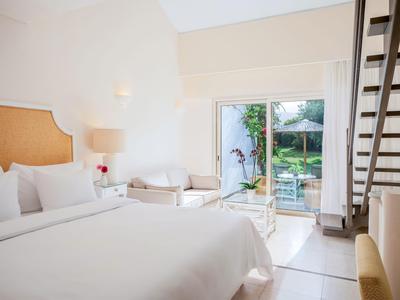 Camera d'hotel luminosa con letto matrimoniale, poltrona, accesso al giardino e design moderno.