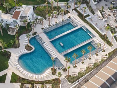 Vista aerea di un hotel con più piscine blu e lettini prendisole.