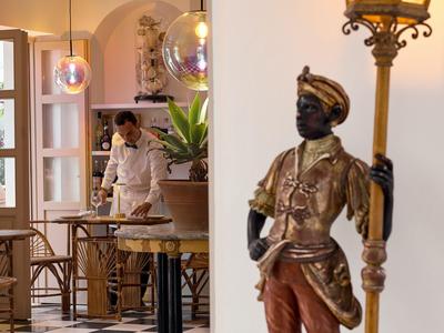 Una figura maschile di colore scuro dipinta d'oro che tiene una lampada in una sala da pranzo di un hotel con tavoli e sedie.