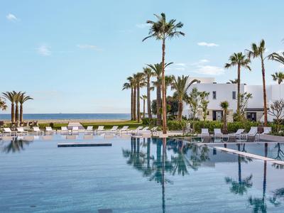 Piscina moderna con lettini e palme davanti a un edificio bianco dell'hotel vicino al mare.
