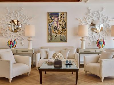 Soggiorno elegante con divano beige, due poltrone, due lampade e un dipinto astratto.