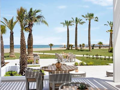 Terrazza con tavolo e sedie, vista su palme e mare sullo sfondo soleggiato.