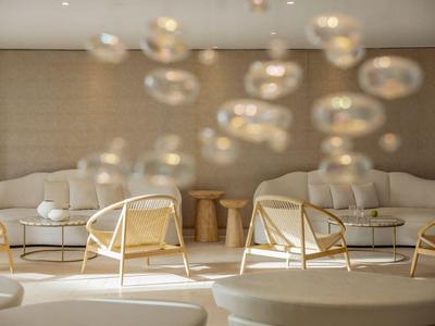 Area lounge di un hotel moderno con poltrone eleganti, divani e tavoli rotondi in legno dai toni caldi.