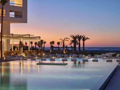 Piscina moderna dell'hotel con lettini e palme al tramonto vicino al mare.