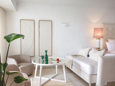 Camera d'hotel moderna con letto bianco, poltrona accogliente e tavolo con decorazioni.