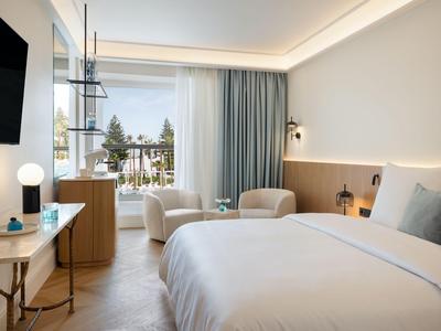 Camera d'hotel moderna con letto matrimoniale, poltrone e balcone con vista sugli alberi.