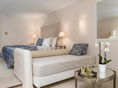 Habitación de hotel luminosa con cama doble, sofá cama y orquídea decorativa sobre una mesa redonda.