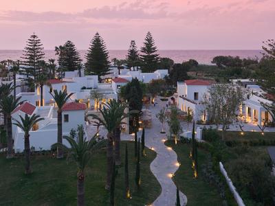 Complesso alberghiero con edifici bianchi e sentiero illuminato al tramonto vicino al mare.