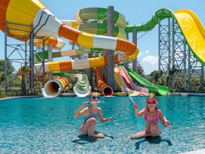 Due donne siedono al bordo di una piscina con grandi scivoli d'acqua colorati sullo sfondo.