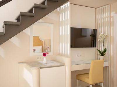 Área moderna de habitación de hotel con TV, silla amarilla y decoración bajo una escalera.