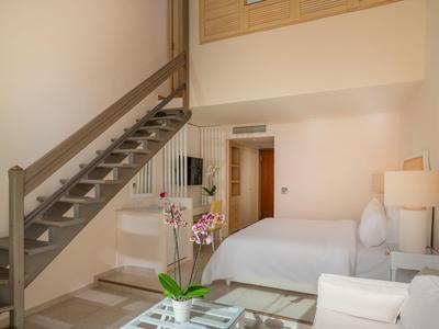 Habitación de hotel luminosa con cama doble, escalera a entrepiso y muebles modernos.