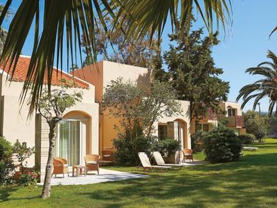 Complejo hotelero con bungalows en fila, césped verde y palmeras en un día soleado