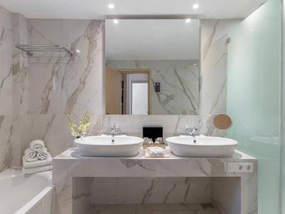 Baño moderno con dos lavabos, gran espejo de pared y bañera con azulejos de mármol.