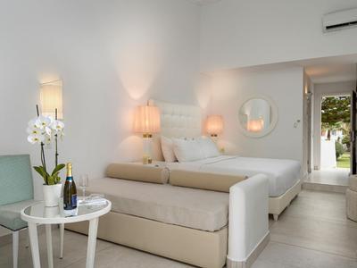 Camera d'albergo luminosa con letto matrimoniale, panca, comodini e porta verso l'esterno.