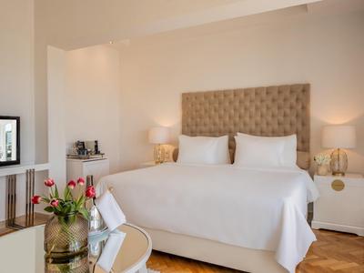 Camera d'hotel elegante con letto grande, biancheria bianca, comodini e illuminazione accogliente.