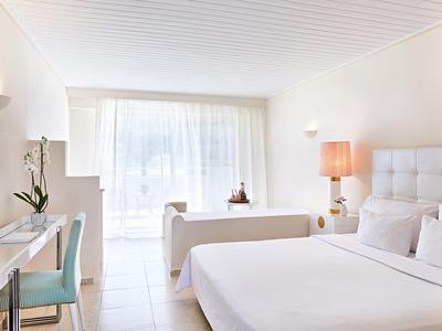 Habitación luminosa con cama grande, sofá, escritorio y ventana con cortinas.