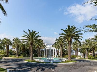 Hotel con edificio blanco, palmeras y fuente bajo cielo azul