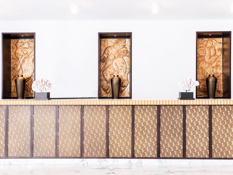 Recepción de hotel moderna con mostrador decorativo y obras de arte detrás de tres ventanas.