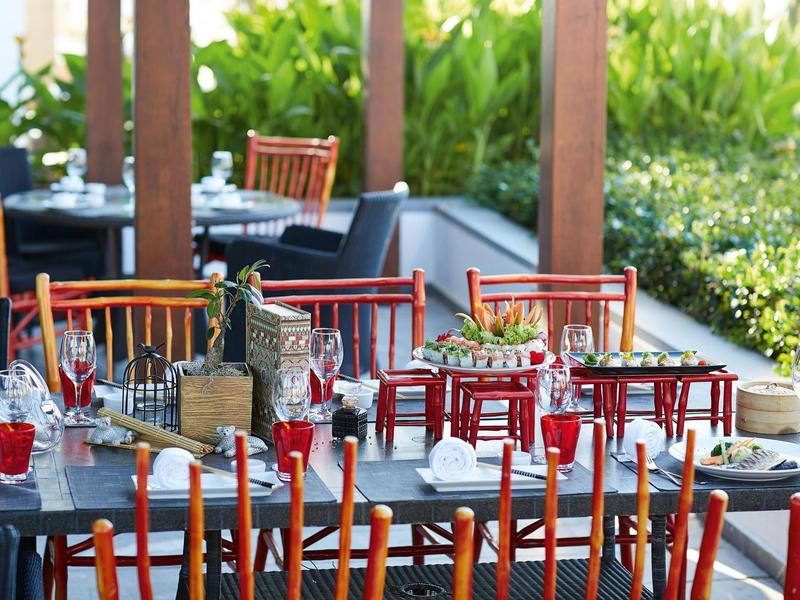 Mesas preparadas con sillas rojas en una terraza con plantas de fondo