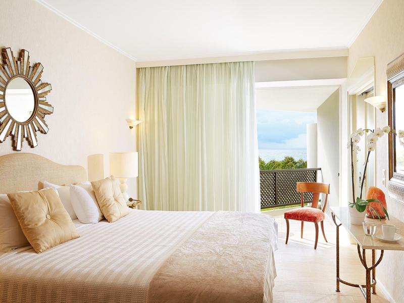 Habitación de hotel luminosa con cama doble, espejo, silla y balcón con vista.