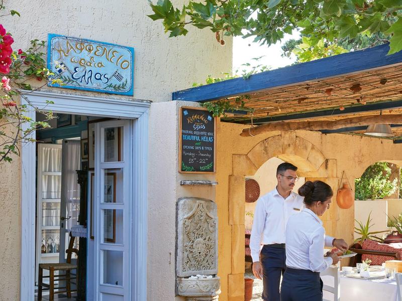 Dos camareros frente a un restaurante rústico con puerta azul y blanca y menú colgante