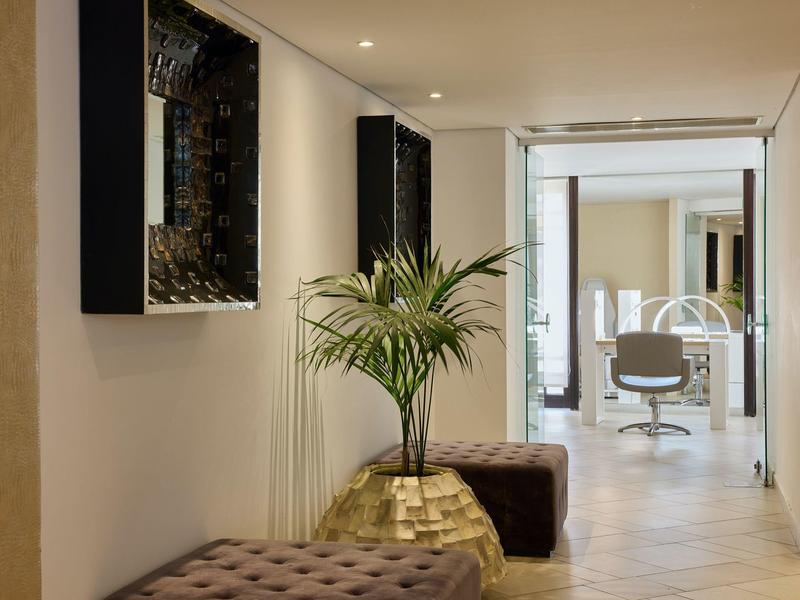 Vista a través de un pasillo luminoso del hotel con plantas y asientos hacia la recepción.