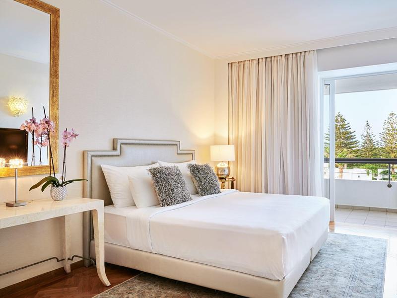 Habitación de hotel moderna con cama doble, lámparas de noche y balcón con vista a áreas verdes.