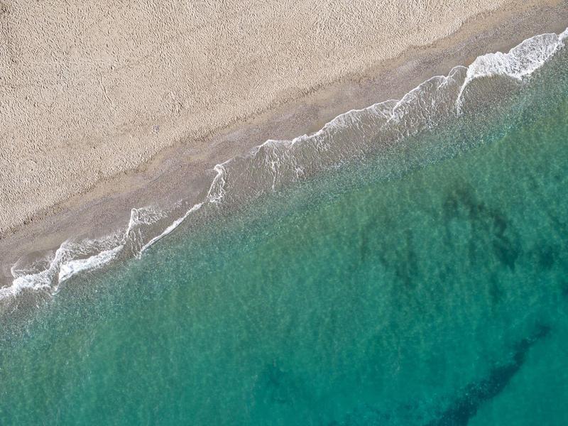 Vista aérea de una playa tranquila con agua azul verdosa clara y olas suaves.
