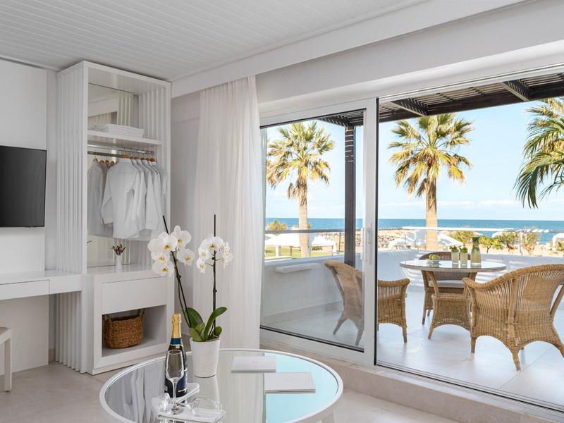 Habitación de hotel luminosa con balcón, vista al mar, palmeras y mobiliario moderno