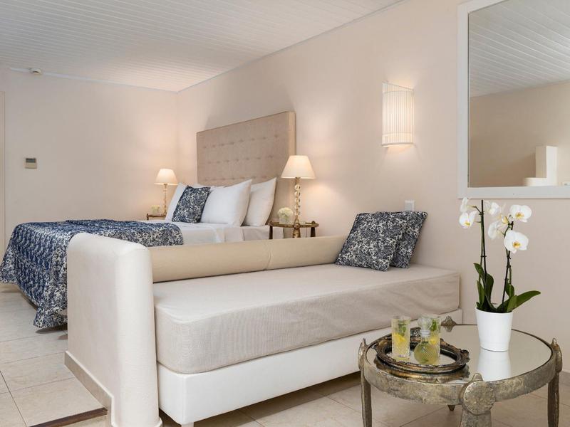 Habitación de hotel luminosa con cama doble, sofá cama y orquídea decorativa sobre una mesa redonda.