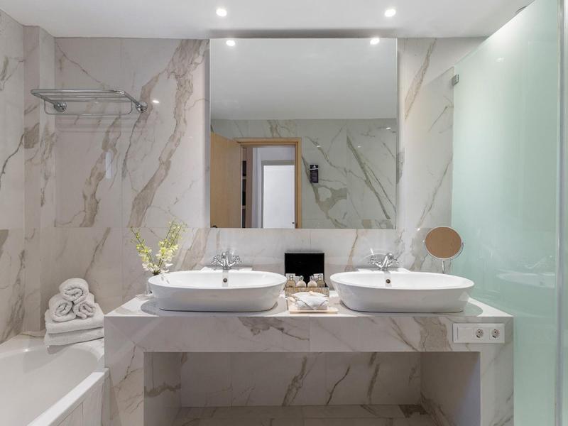 Baño moderno con dos lavabos, gran espejo de pared y bañera con azulejos de mármol.