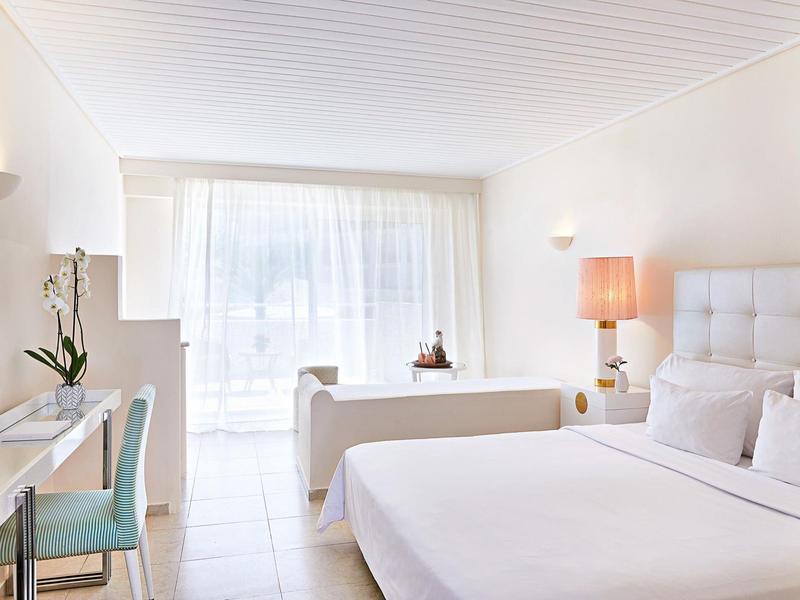 Habitación luminosa con cama grande, sofá, escritorio y ventana con cortinas.