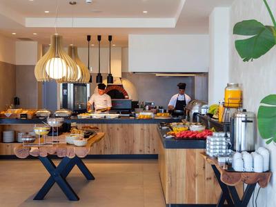 Buffet d'hôtel moderne avec divers plats et deux chefs dans une cuisine ouverte.