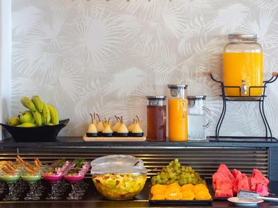 Buffet avec fruits frais, jus et desserts sur une table devant du papier peint.