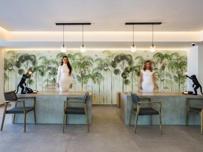 Intérieur de restaurant moderne avec mur de palmiers, deux tables à manger et deux femmes en robes blanches.