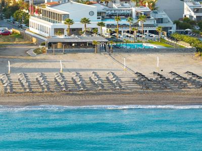 Hotel complex with pool and sun loungers on a sandy beach by turquoise sea.