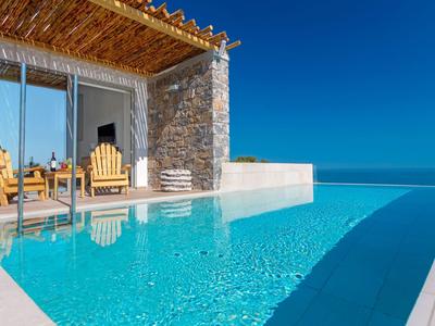 Modern hotel pool with infinity edge and cozy seating area under clear sky.