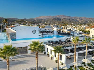 Modern hotel pool with sun loungers, palm trees, and mountains in the background under clear sky.