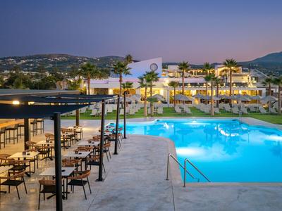 Hotel with outdoor pool, terrace, and illuminated seating areas at dusk.