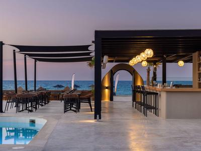 Modern outdoor area with pool, bar, and sea view at sunset.