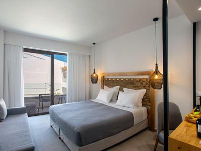 Modern hotel room with double bed, sofa, and balcony overlooking the city.