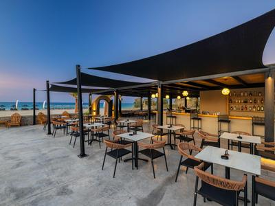 Open beach bar area with tables and chairs at sunset by the sea.