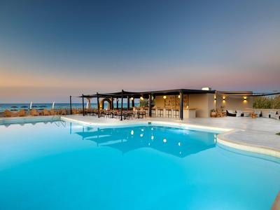 Modern hotel pool with clear water and lounge area at sunset.