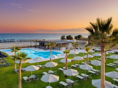 Hotel beach with lounge chairs, umbrellas, pool, and calm sea view at sunset.