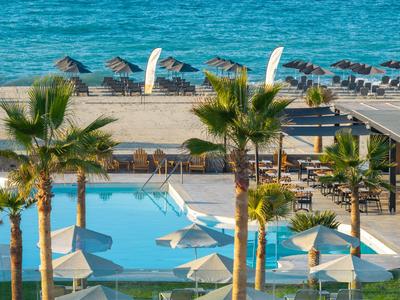 Hotel pool with white sun umbrellas and palm trees on the beach by calm sea.